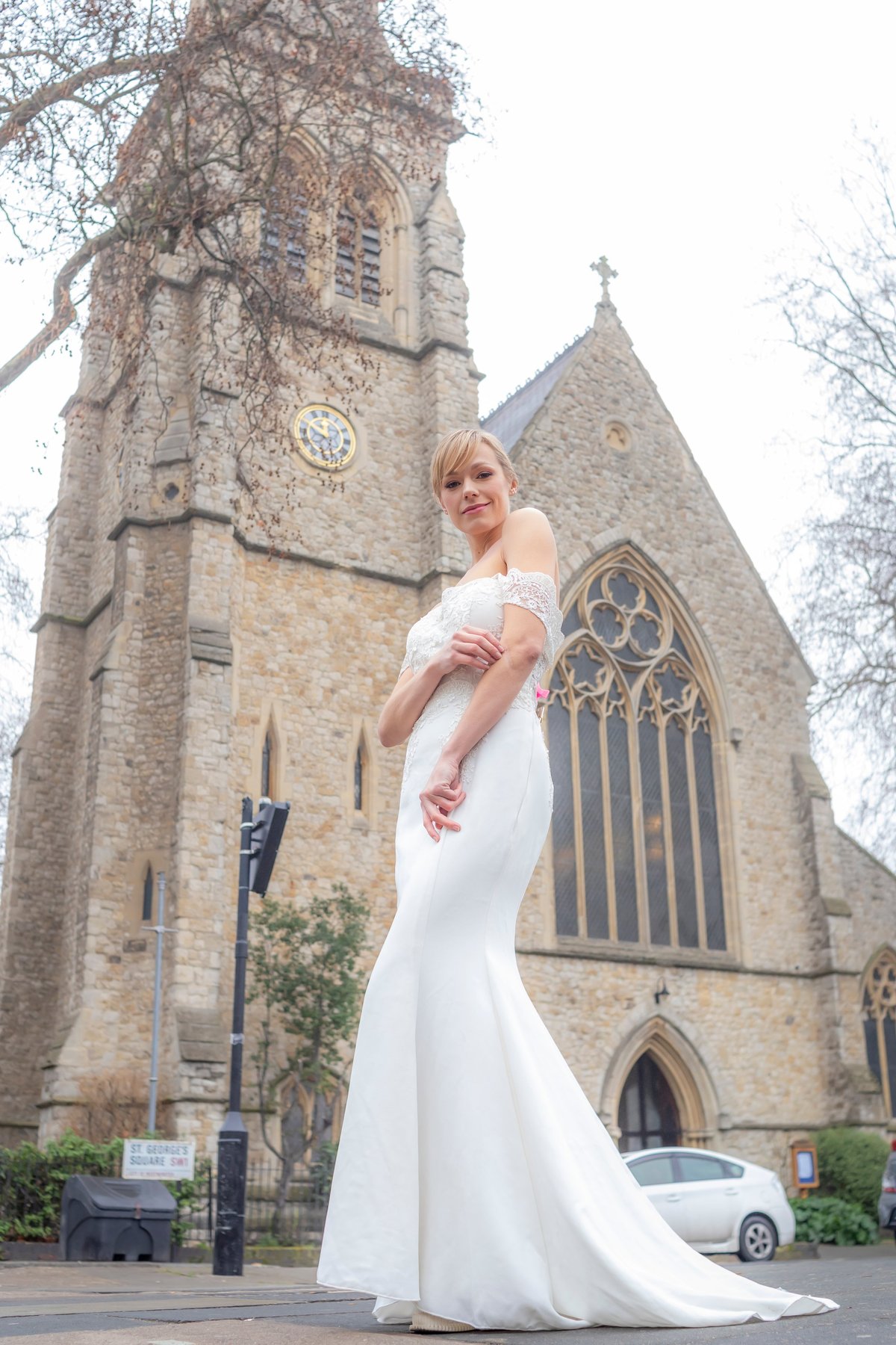 Noiva de vestido branco posando em frente a igreja de pedra com torre de relógio