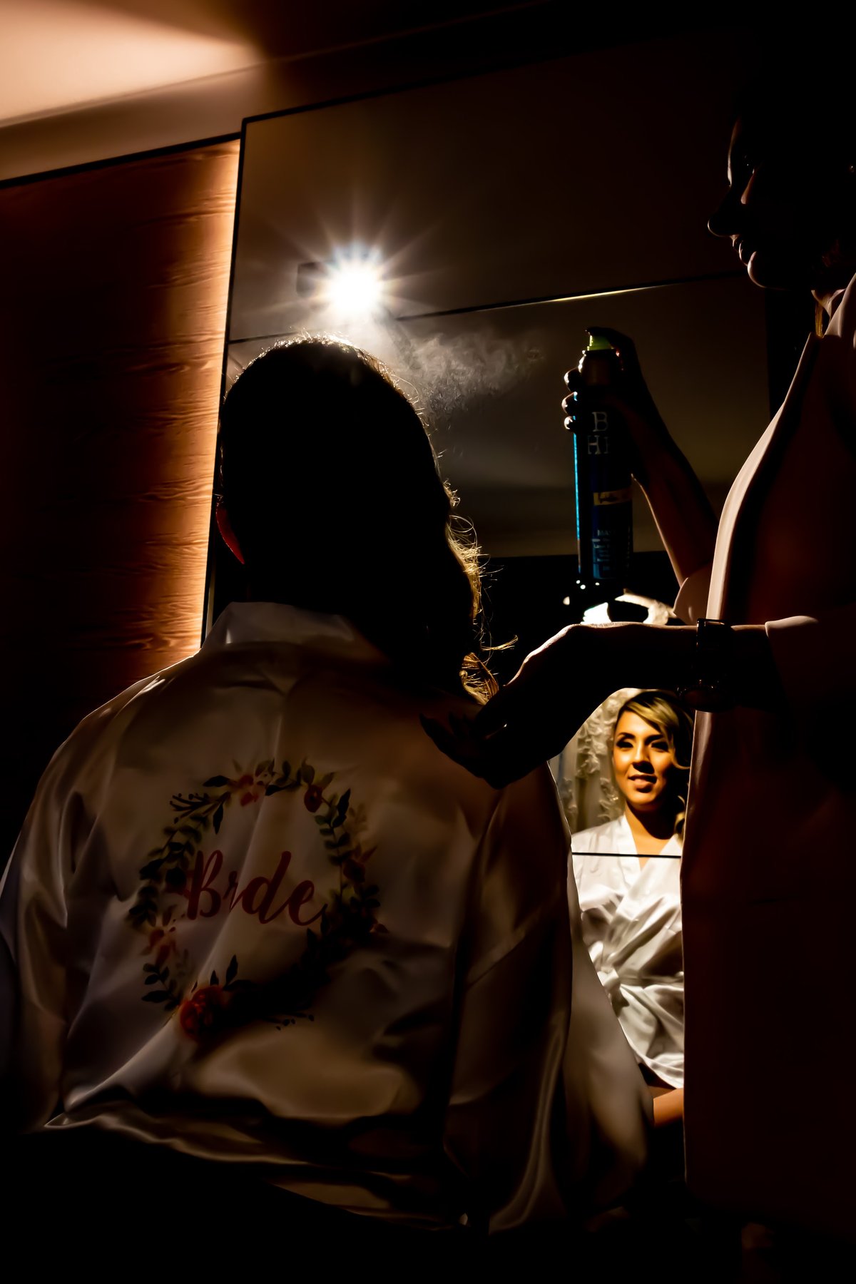 Noiva de robe bordado com palavra Bride ajustando o cabelo no espelho com iluminação forte de estúdio