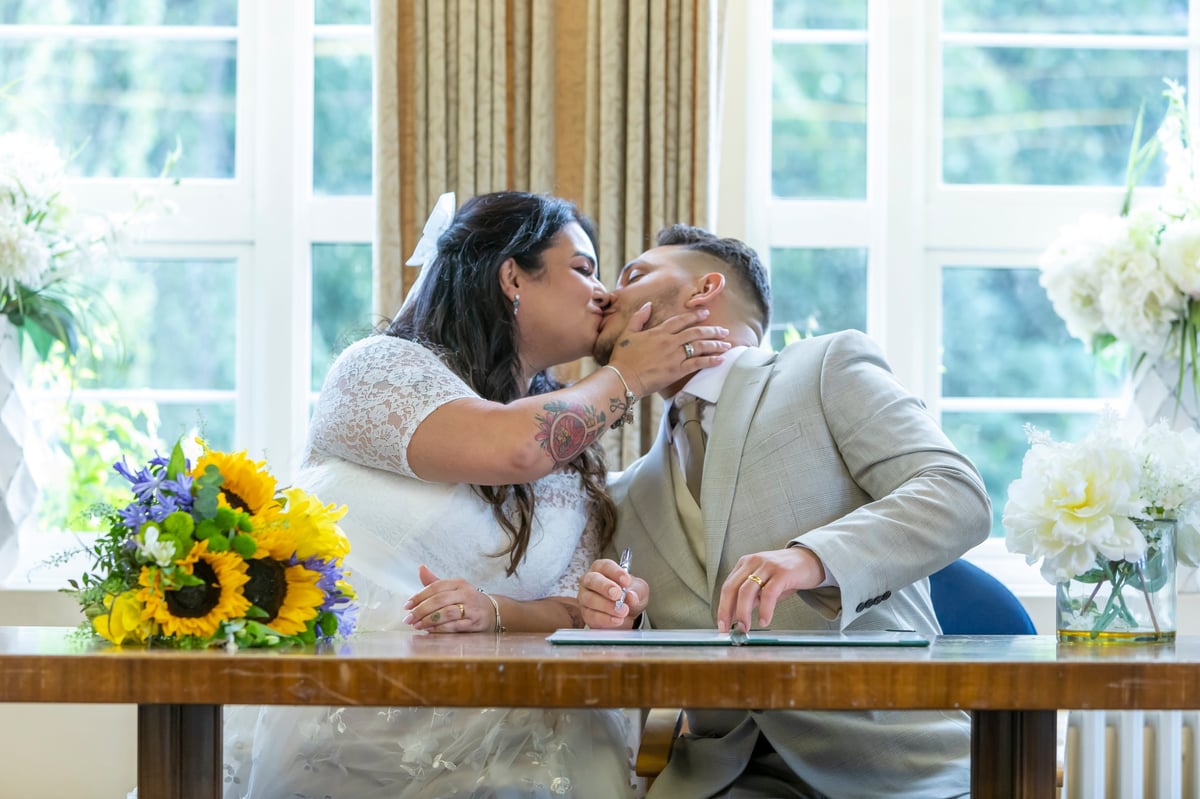Noiva e noivo se beijando à mesa com girassóis em ambiente claro e elegante