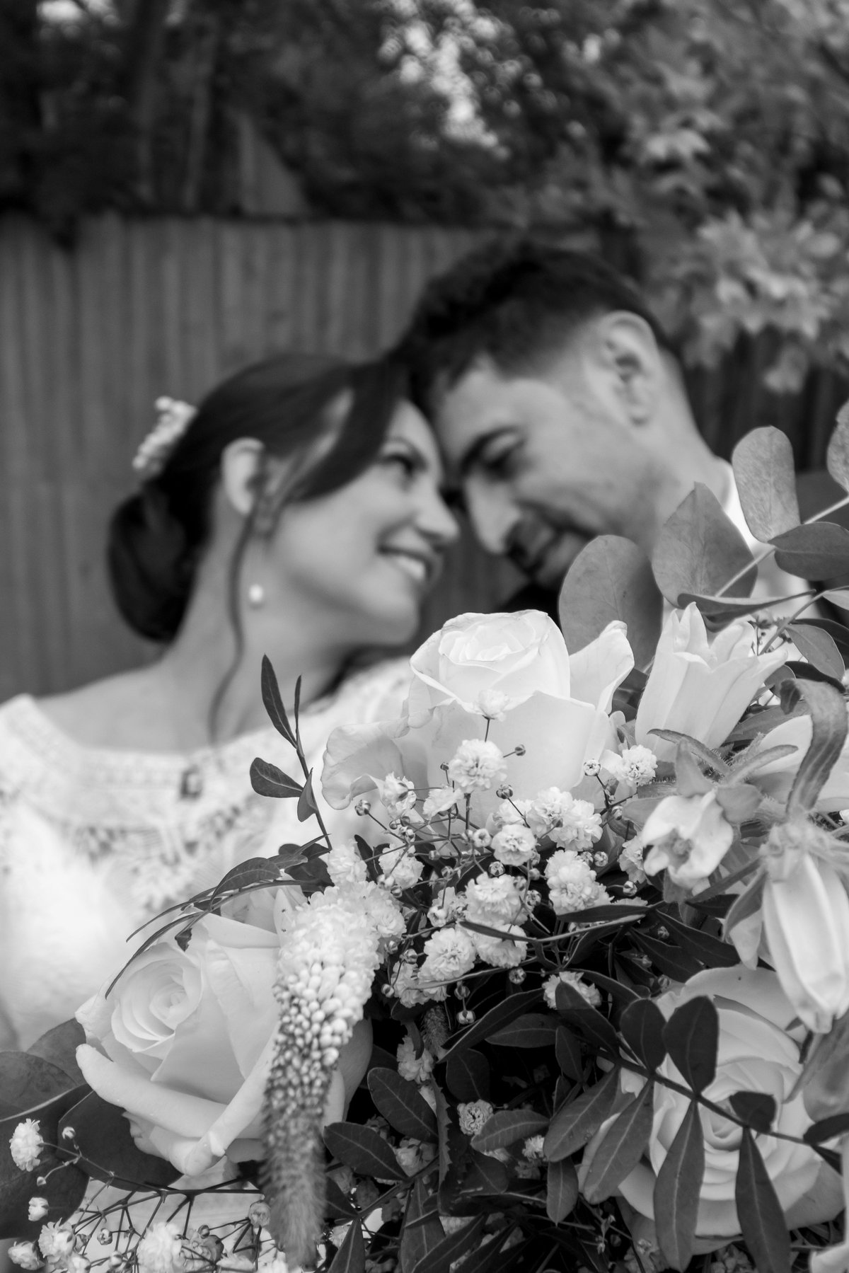 Foto em preto e branco dos noivos sorrindo com buquê de rosas e flores brancas