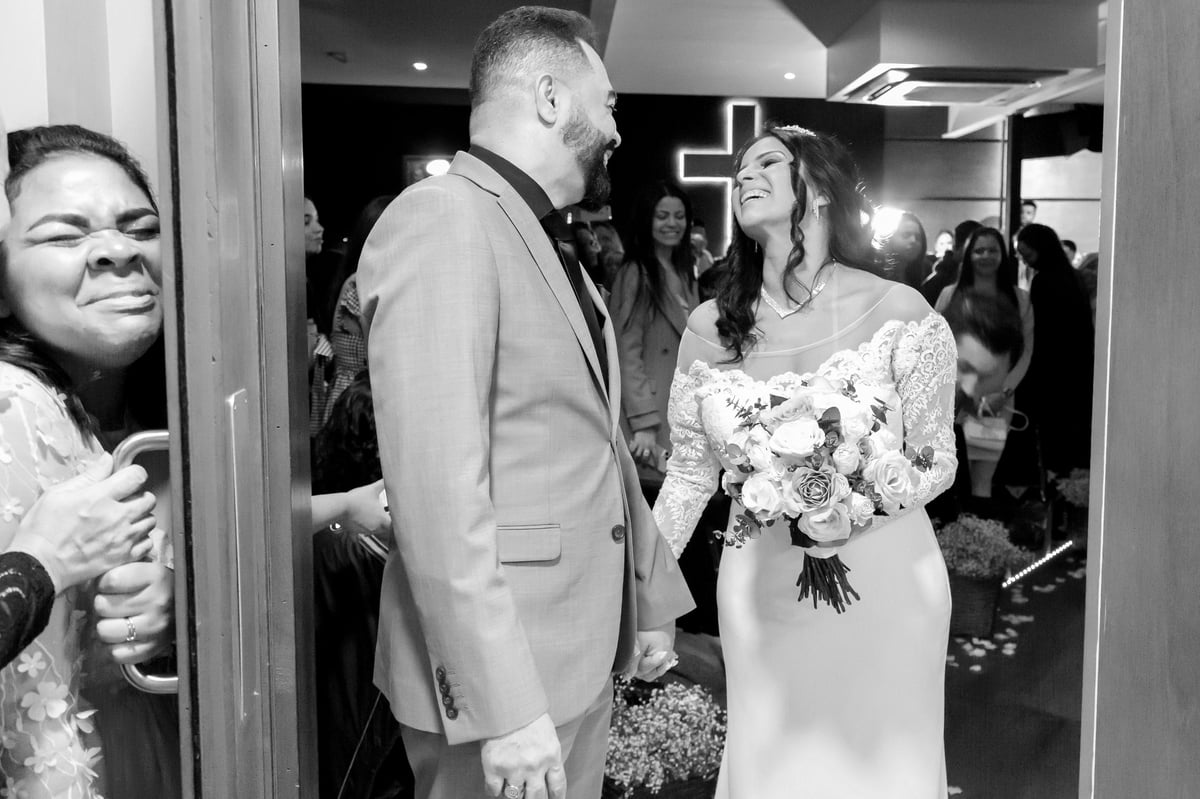 Foto em preto e branco da noiva e do noivo conversando com convidados na recepção do casamento