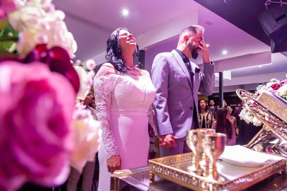 Casal na recepção de casamento com arranjos florais rosas e iluminação ambiente em tons rosados